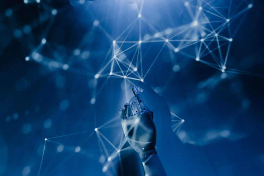 robot-pointing-on-a-wall-8386440 A robotic hand reaching into a digital network on a blue background, symbolizing AI technology.